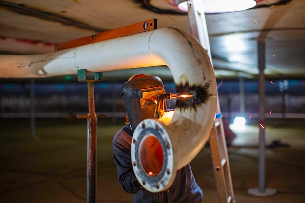 Foto scintilla di taglio del gomito della tubazione metallica del lavoratore maschio sul serbatoio con il lampo della luce di taglio da vicino indossare guanti e maschera protettivi