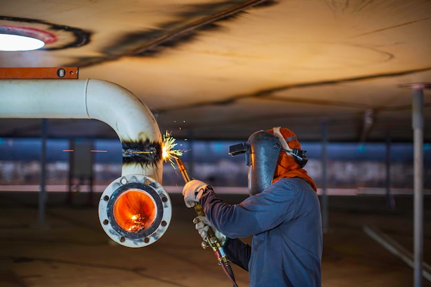 Male worker metal pipeline elbow cutting spark on the tank with the flash of cutting light close up wear protective gloves and mask