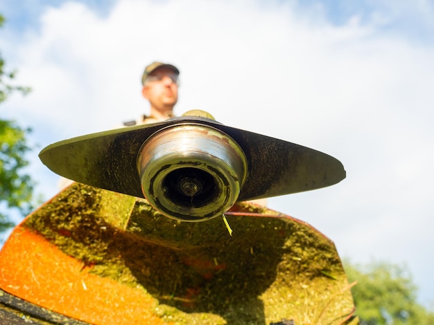 A male worker mows the grass with a gasoline trimmer bottom view selective focus on the trimmer blade