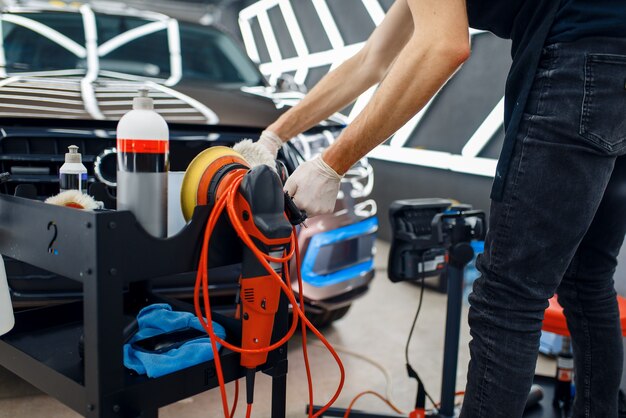 Male worker near toolbox with polishing machine and polish tools, car detailing. Preparationa before installation of coating that protects the paint of automobile from scratches, auto tuning