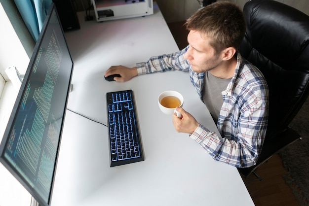 Un lavoratore maschio in ufficio con una tazza di bevanda calda seduto davanti al computer