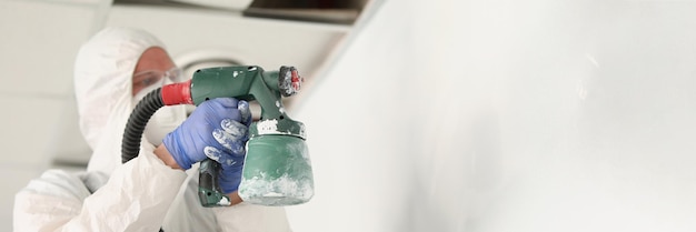 Male worker painting wall with spray gun in white colour busy handyman at work