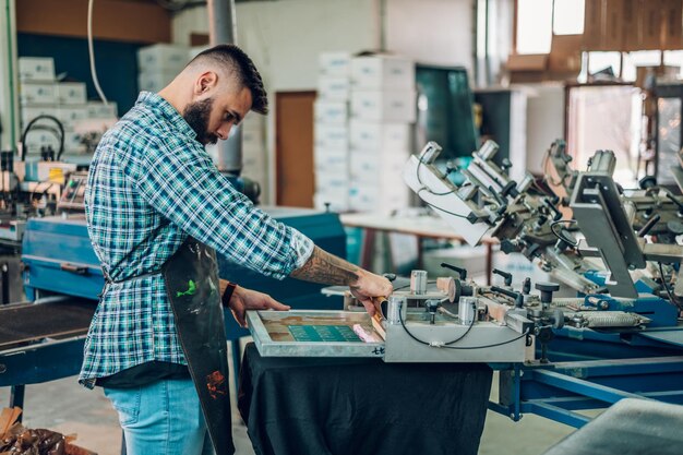 Male worker pressing ink on frame while using the printing\
machine in a workshop