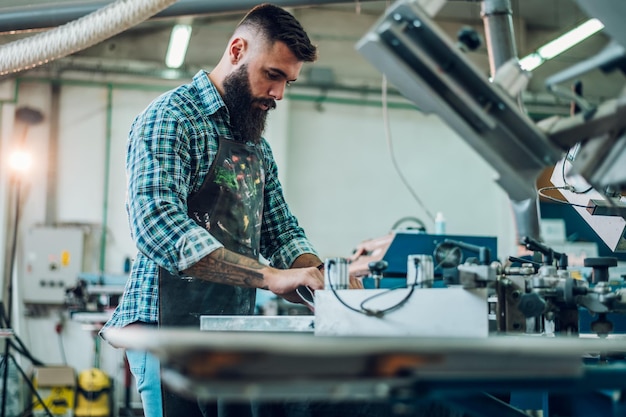 Male worker pressing ink on frame while using the printing
machine in a workshop