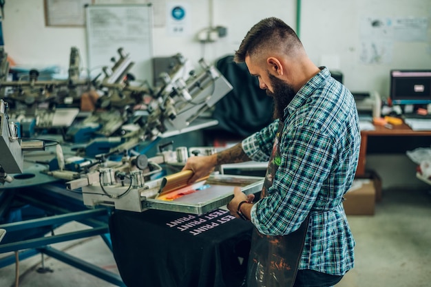 Male worker pressing ink on frame while using the printing\
machine in a workshop