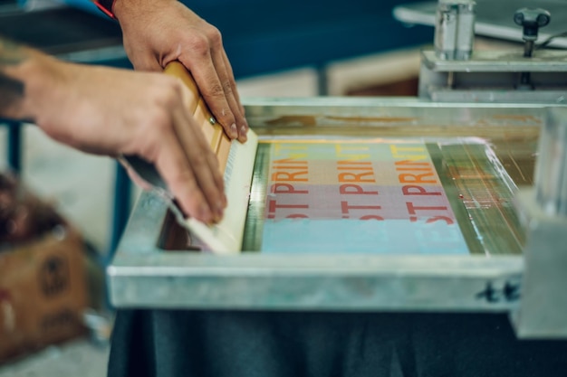 Foto operaio maschio che preme inchiostro sul telaio durante l'utilizzo della macchina da stampa in un'officina