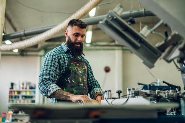 Male worker pressing ink on frame while using the printing\
machine in a workshop