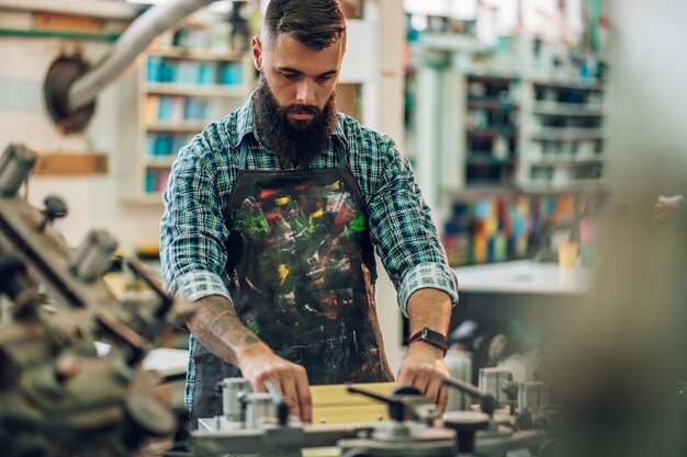 Male worker pressing ink on frame while using the printing\
machine in a workshop