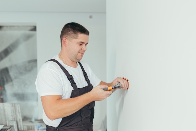 Male worker professional electrician installs electrical outlet in apartment after repair