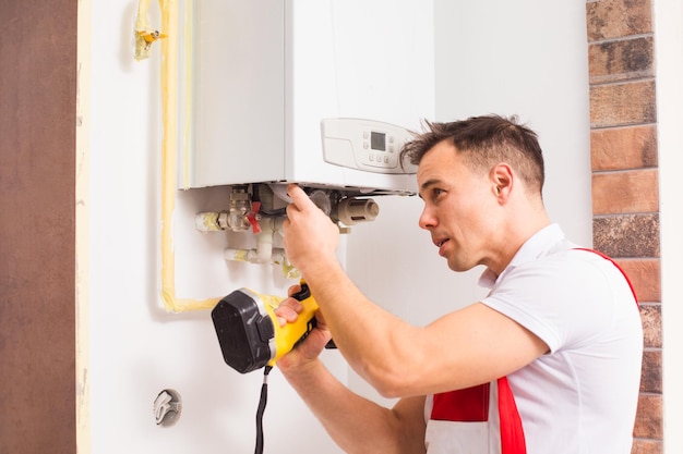 Male worker repairs the boiler Plumber in overalls while working side view