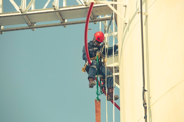 Male worker rope access industrial working at height tank oil\
wearing harness, helmet safety equipment rope access inspection of\
thickness tank oil and gas.