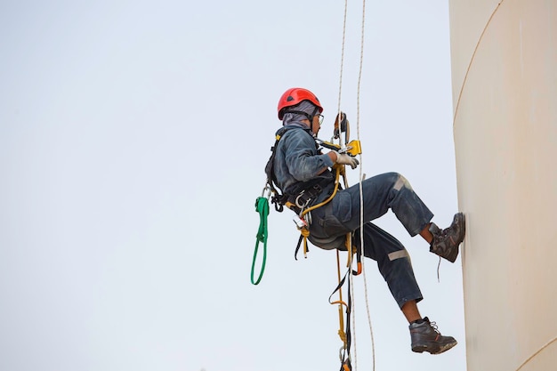 Foto lavoratore maschio accesso su fune lavoro industriale ad altezza serbatoio olio che indossa imbracatura casco equipaggiamento di sicurezza accesso su fune ispezione del serbatoio di spessore