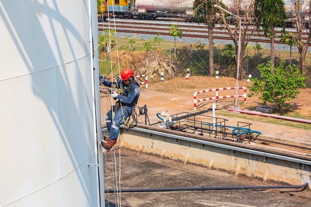 Male worker rope access industrial working at height tank oil\
wearing harness helmet safety equipment rope access inspection of\
thickness tank