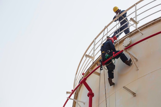 Male worker rope access industrial working at height tank oil wearing harness helmet safety equipment rope access inspection of thickness tank