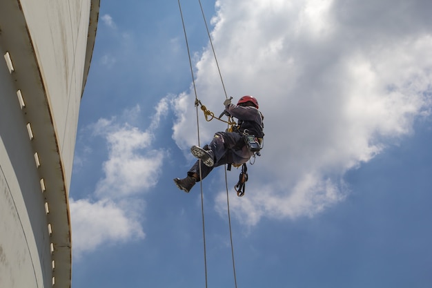 Male worker rope access  inspection of thickness storage tank industry background blue sky