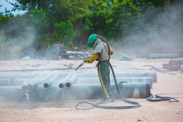 Male worker Sand blasting process cleaning pipeline surface on steel before painting in factory.