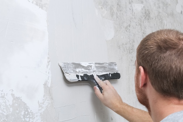 A male worker spreads the putty mixture and flattens wall