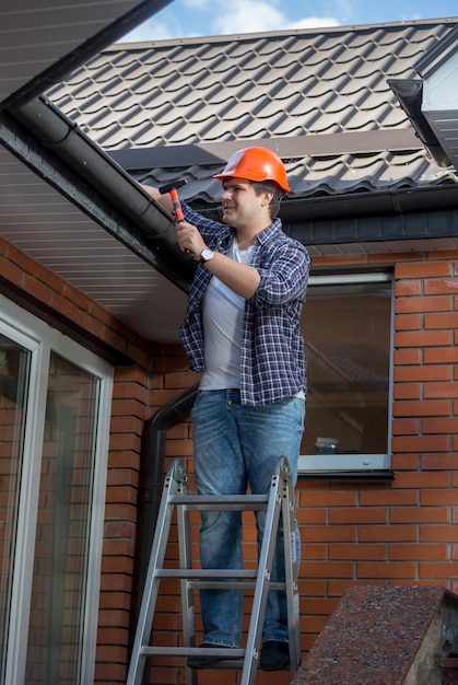 Male worker standing on step ladder in front of house