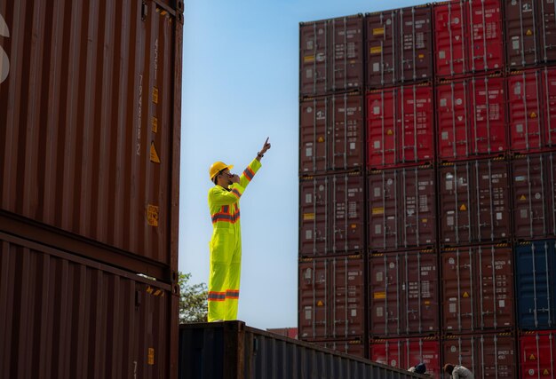 A male worker stands on a container box while wearing a safety suit Use the walkie talkie