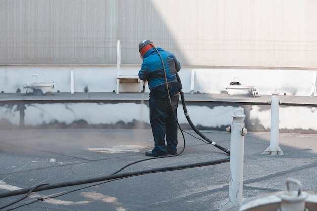 Photo male worker surface corrosion roof plate preparation by sand blasting of tank