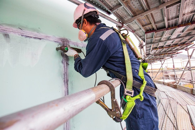 Male worker test steel tank butt weld carbon shell plate of\
storage tank oil magnetic field test work at height full body\
harness