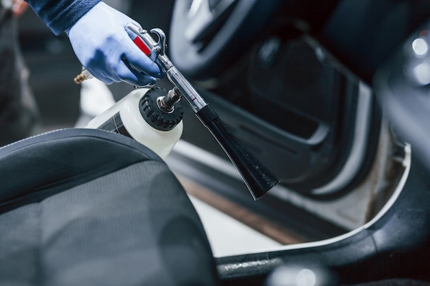 Male worker in uniform cleaning new modern car Conception of service