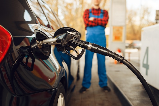 Male worker in uniform fuels vehicle on gas station