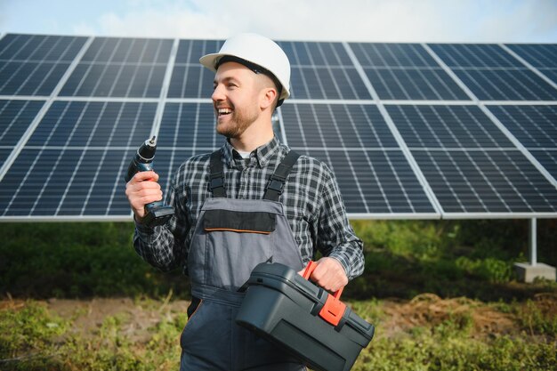 Male worker in uniform outdoors with solar batteries at sunny day