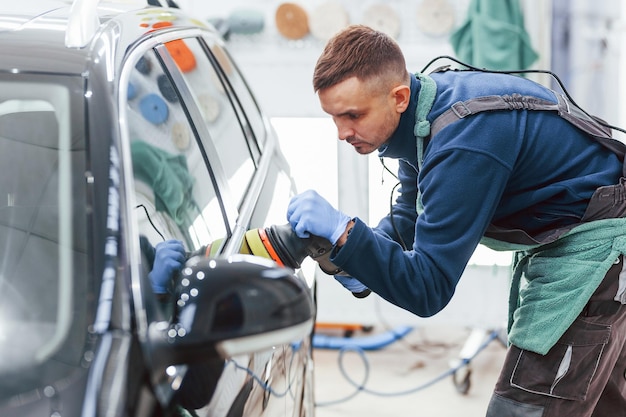 Male worker in uniform polishing new modern car Conception of service