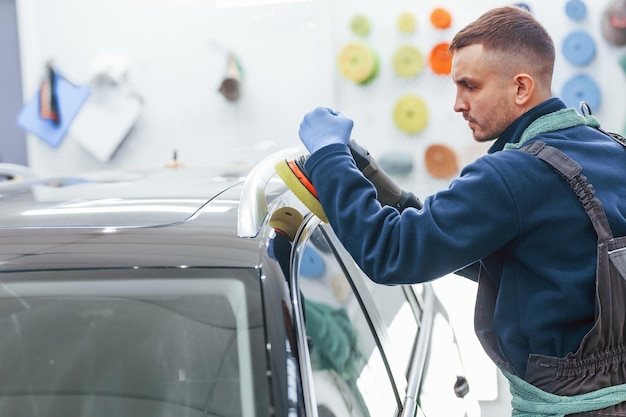 Male worker in uniform polishing new modern car Conception of service