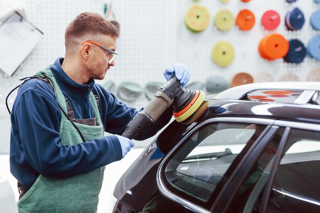 Male worker in uniform polishing new modern car Conception of service