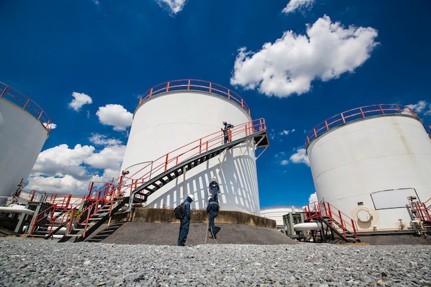 Male worker walking the stairway industry visual inspection storage tank oil cloudy blue sky.