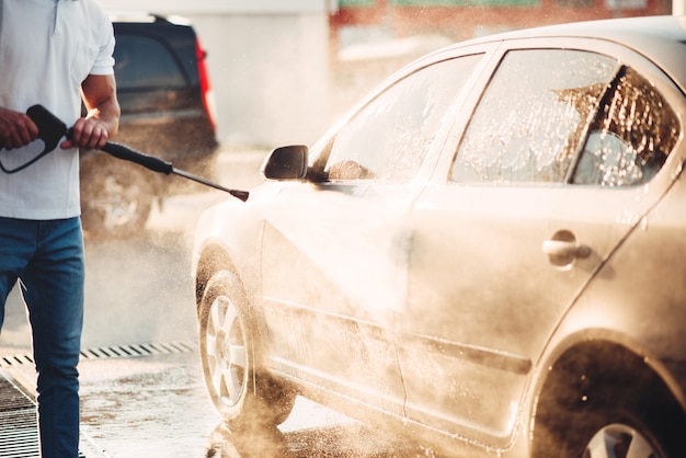 Male worker wash the car with high pressure washer. Car-wash station