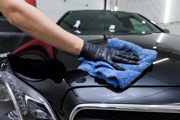 Photo a male worker washes a black car wiping water with a soft cloth and microfiber cleaning the surface to shine in a vehicle detailing workshop auto service industry