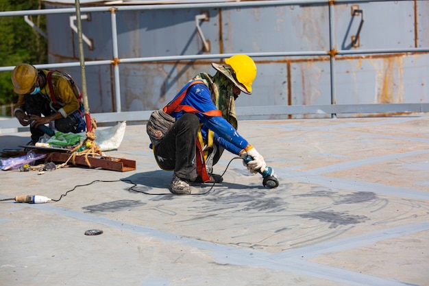 Male worker wearing protective clothing cleaning roof oil storage tank industrial construction