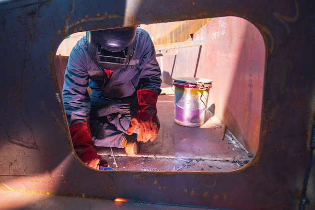 Foto lavoratore di sesso maschile che indossa indumenti protettivi e ripara il pontone tombino saldatura fumo costruzione industriale olio galleggiante serbatoio di stoccaggio all'interno di spazi ristretti.