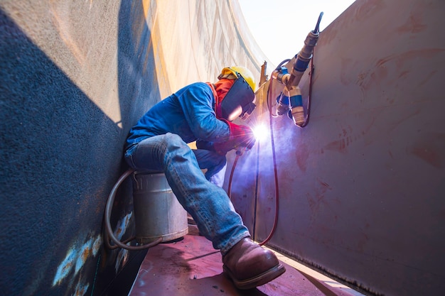 Male worker wearing protective clothing and repair welding industrial construction oil and gas or storage tank inside confined spaces.