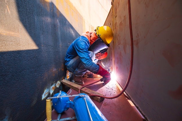 防護服を着用し、限られたスペース内で工業用建設の石油とガスまたは貯蔵タンクを修理溶接する男性労働者。