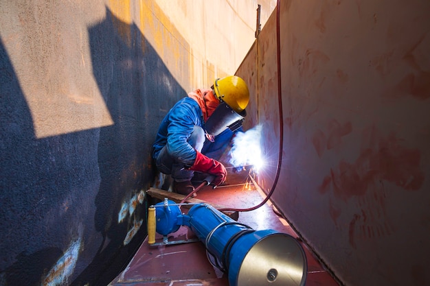 Male worker wearing protective clothing and repair welding industrial construction oil and gas or storage tank inside confined spaces.