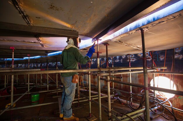 Male worker wearing protective clothing and repair welding industrial construction oil and gas or storage tank inside confined spaces.