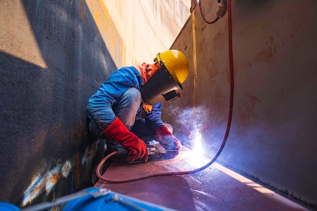 Lavoratore di sesso maschile che indossa indumenti protettivi e ripara saldatura di petrolio e gas da costruzione industriale o serbatoio di stoccaggio all'interno di spazi ristretti.