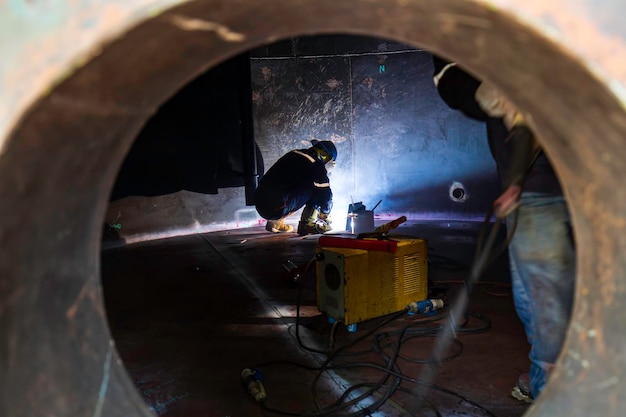 防護服を着て溶接を修理する男性労働者は、限られたスペース内で産業建設タンクコイルの重油をスパークさせます。