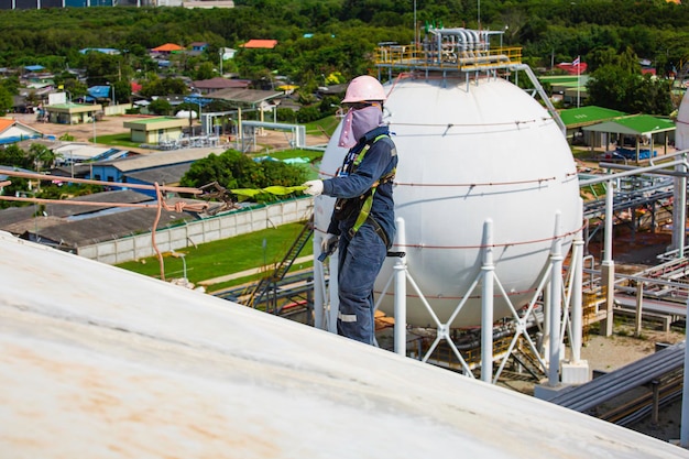 Male worker wearing safety first harness rope safety line\
working at a high place on tank spherical gas propane