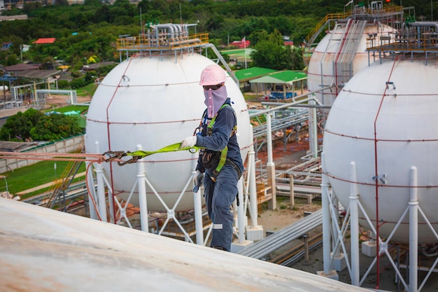 Male worker wearing safety first harness rope safety line working at a high place on tank spherical gas propane