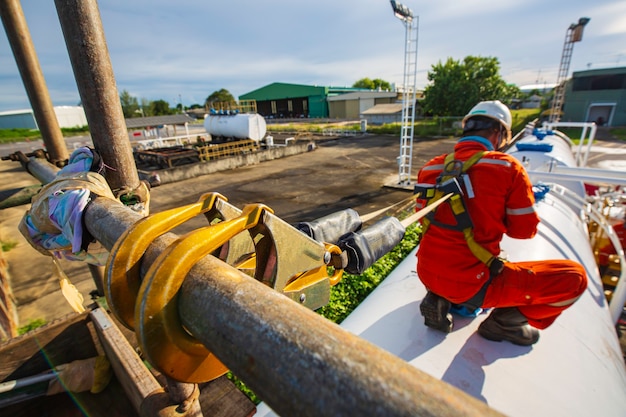 Male worker wearing safety first harness and safety lone working at high scaffold place on open top tank roof oil