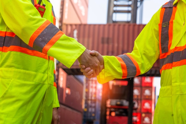 Male worker wearing a uniform loads a container shaking hands with a colleague engineer