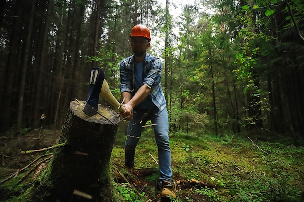 Рабочий-мужчина рубит дерево в лесу топором.
