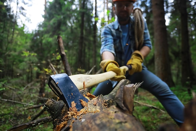 Foto lavoratore maschio con un'ascia che taglia un albero nella foresta