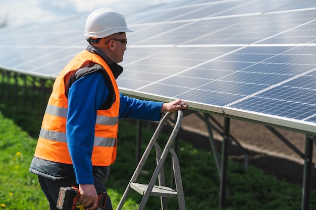 Male worker with drill screwdriver climbs the stepladder to the solar panels