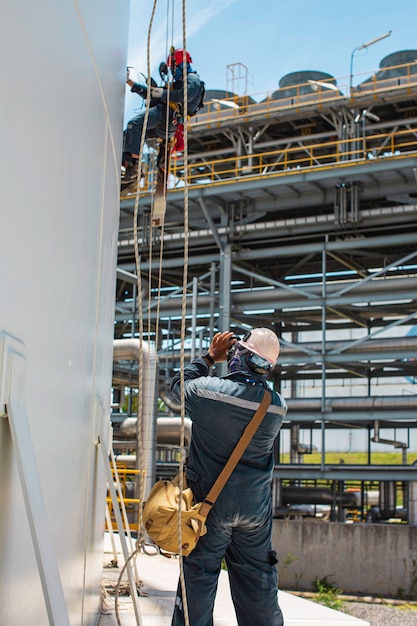 男性労働者は、高さでの厚さシェルプレート貯蔵タンクの安全作業のロープダウンハイトタンクロープアクセス検査を制御します。